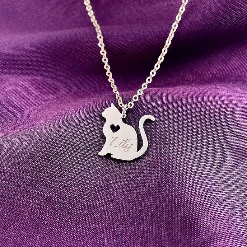 Pode incluir: Colar de prata com um pingente com a silhueta de um gato. O pingente tem um pequeno cora&ccedil;&atilde;o recortado e o nome "Lily" gravado.