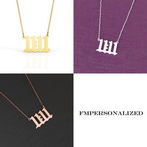 May include: A gold-colored necklace with the number 11:11 pendant. The necklace is displayed on a white background. The pendant is in a gothic font. The image also shows a silver and a rose gold necklace with the same pendant.
