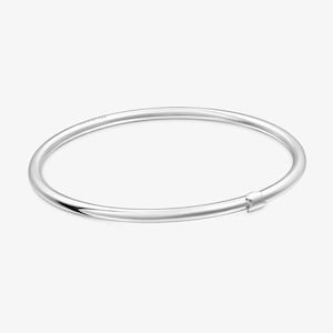 Puede incluir: Una pulsera de brazalete plateada con un diseño simple y minimalista. La pulsera es un círculo completo con un pequeño cierre. La joya está hecha de un metal brillante y reflectante.