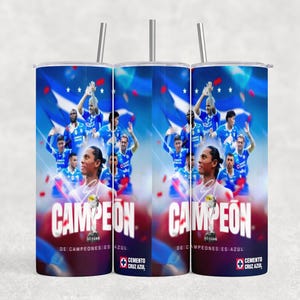 May include: A cylindrical tumbler with a metal straw featuring a blue graphic design of a soccer team celebrating a victory. The text CAMPEON DE CAMPEONES ES AZUL is printed in white, along with the Cemento Cruz Azul logo at the bottom of the cup.