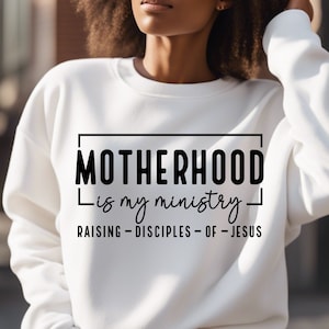 May include: White sweatshirt with black text that reads "MOTHERHOOD is my ministry - RAISING - DISCIPLES - OF - JESUS".