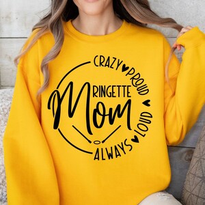 May include: Yellow sweatshirt with a black circle design that says "Crazy Proud Ringette Mom Always Loud" with hearts around the text.