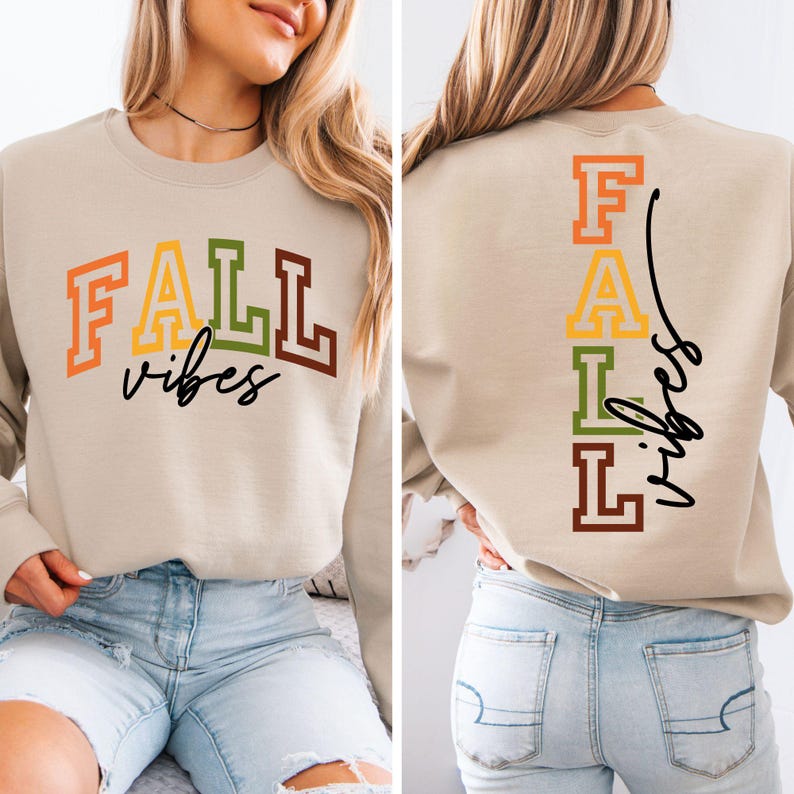 May include: Beige sweatshirt with the words "FALL vibes" in orange, yellow, green, and brown block letters. The back of the sweatshirt has the word "FALL" vertically in the same colors, with "vibes" in black script.