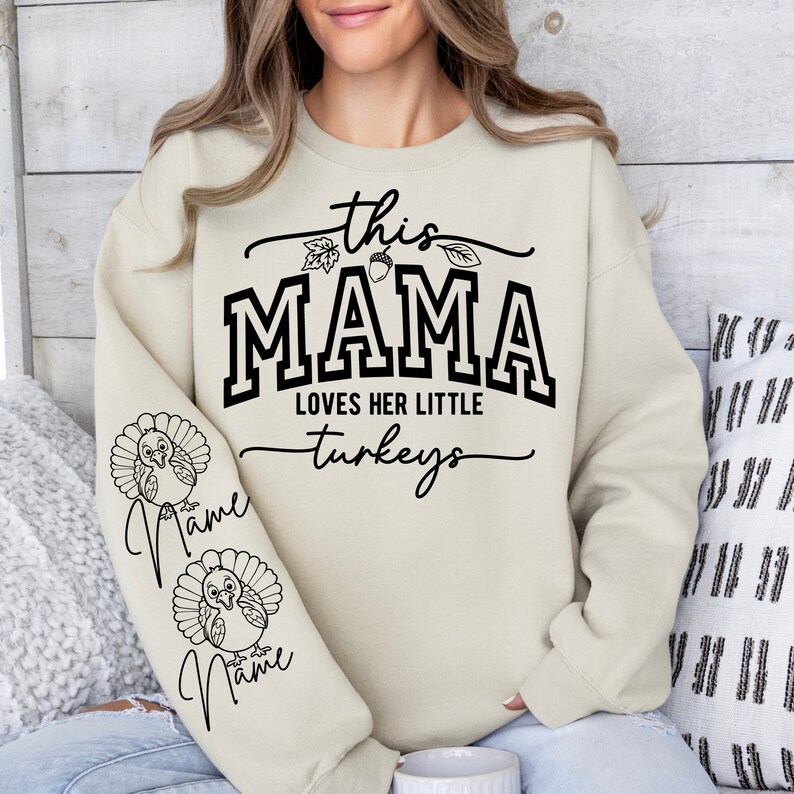 May include: A beige sweatshirt with the text "this mama loves her little turkeys" and two turkeys on the sleeves. The text "Name" is written below each turkey.