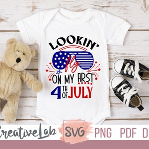 May include: White baby bodysuit with the text "Lookin' Fly on my First 4th of July" in red, white, and blue. The design includes sunglasses with a star-filled lens. A teddy bear and black and white baby shoes are next to the bodysuit.