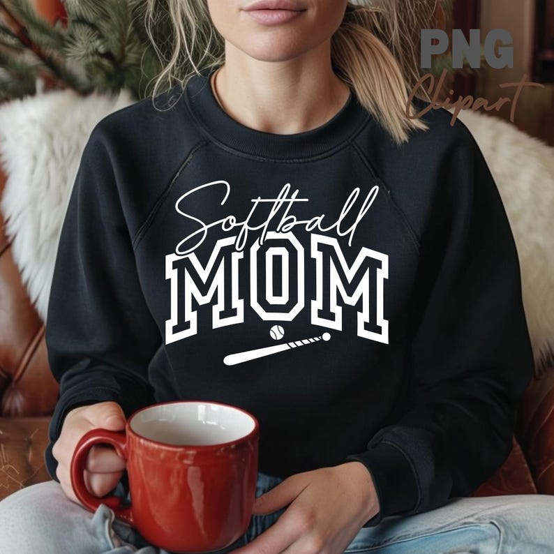 May include: Black sweatshirt with the words "Softball MOM" in white script and block letters, along with a baseball and bat graphic. A red mug is held in the hands.