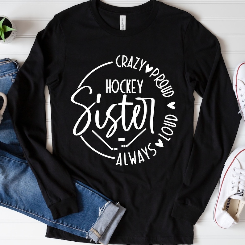 Puede incluir: Camiseta negra de manga larga con un gr&aacute;fico circular blanco que dice "Crazy Hockey Sister Always Proud Loud" con palos de hockey y corazones.