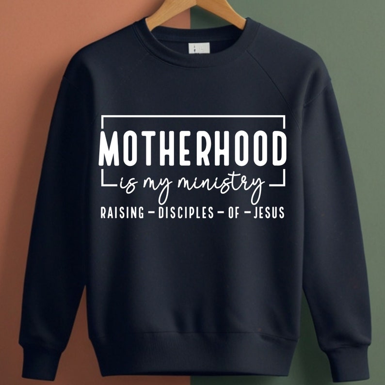 May include: Navy blue sweatshirt with white text that reads "Motherhood is my ministry - Raising Disciples of Jesus".