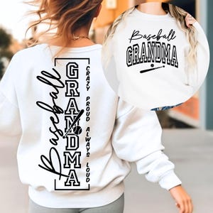 May include: White sweatshirt with the words "Baseball Grandma" in black script and block letters. The back of the sweatshirt has the words "Baseball Grandma" vertically, with a baseball bat and ball graphic. Additional text reads "Crazy, Proud, Always, Loud."