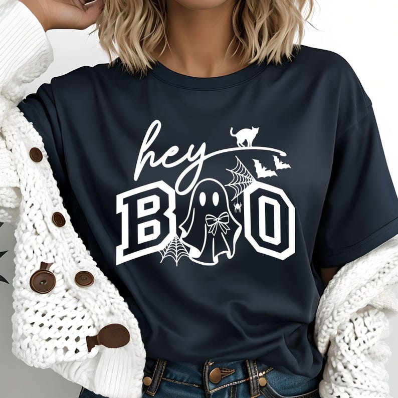 Puede incluir: Camiseta azul marino con la frase blanca "hey BOO". El dise&ntilde;o incluye un fantasma con lazo, telara&ntilde;as, un gato y murci&eacute;lagos. Una prenda casual para el d&iacute;a a d&iacute;a.