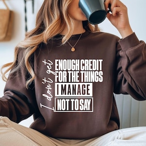 May include: A brown sweatshirt with the text "I don't get enough credit for the things I manage not to say" in white. The sweatshirt is a solid color and has a crew neck.