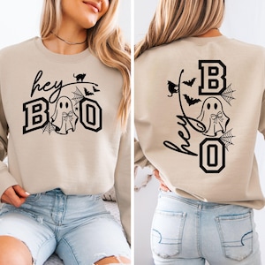 Puede incluir: Sudadera beige con un gr&aacute;fico negro que dice "hey BOO" con un fantasma, telara&ntilde;as, murci&eacute;lagos y un gato. La parte posterior de la sudadera tiene el mismo dise&ntilde;o. Una prenda con tem&aacute;tica de Halloween.