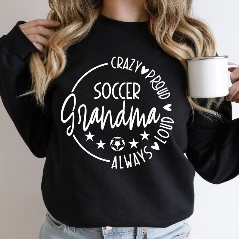 K&ouml;nnte beinhalten: Schwarzes Sweatshirt mit einem wei&szlig;en Kreis-Motiv, auf dem "Crazy Proud Soccer Grandma Always Loud" steht.