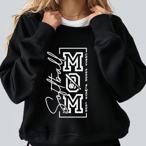May include: Black sweatshirt with the word "Softball" in a cursive font on the left side. The word "MOM" is in a block letter design with a baseball and bat graphic. The text "Crazy, Proud, Always, Loud" is printed vertically on the right.