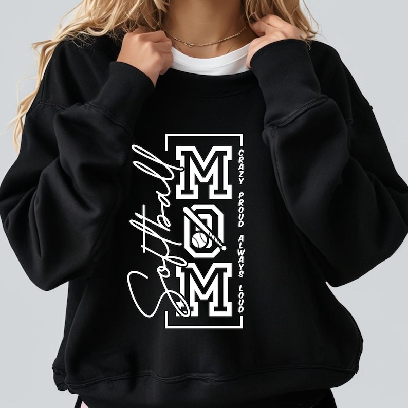 May include: Black sweatshirt with the word "Softball" in a cursive font on the left side. The word "MOM" is in a block letter design with a baseball and bat graphic. The text "Crazy, Proud, Always, Loud" is printed vertically on the right.