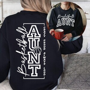 May include: Black sweatshirt with the words "Basketball AUNT" in white script and block letters. The back of the sweatshirt has the words "Basketball AUNT" and a basketball graphic. The words "Crazy Proud Always Loud" are printed vertically.