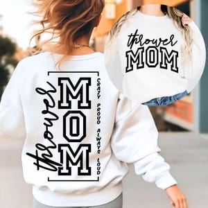 May include: White sweatshirt with the text "Thrower Mom" in black script and block letters. The back of the sweatshirt features the word "Thrower" in script, and the word "MOM" in block letters, with the words "Crazy, Proud, Always, Loud" printed vertically.