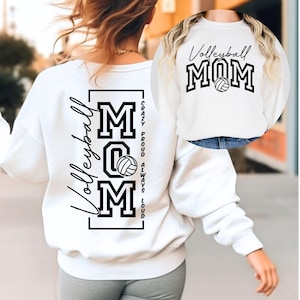 Op de afbeelding: Witte sweatshirt met de tekst "Volleyball MOM" in zwart, met een volleybalafbeelding. De achterkant van de sweatshirt heeft het woord "Volleyball" in script en de woorden "MOM" met een volleybalafbeelding.