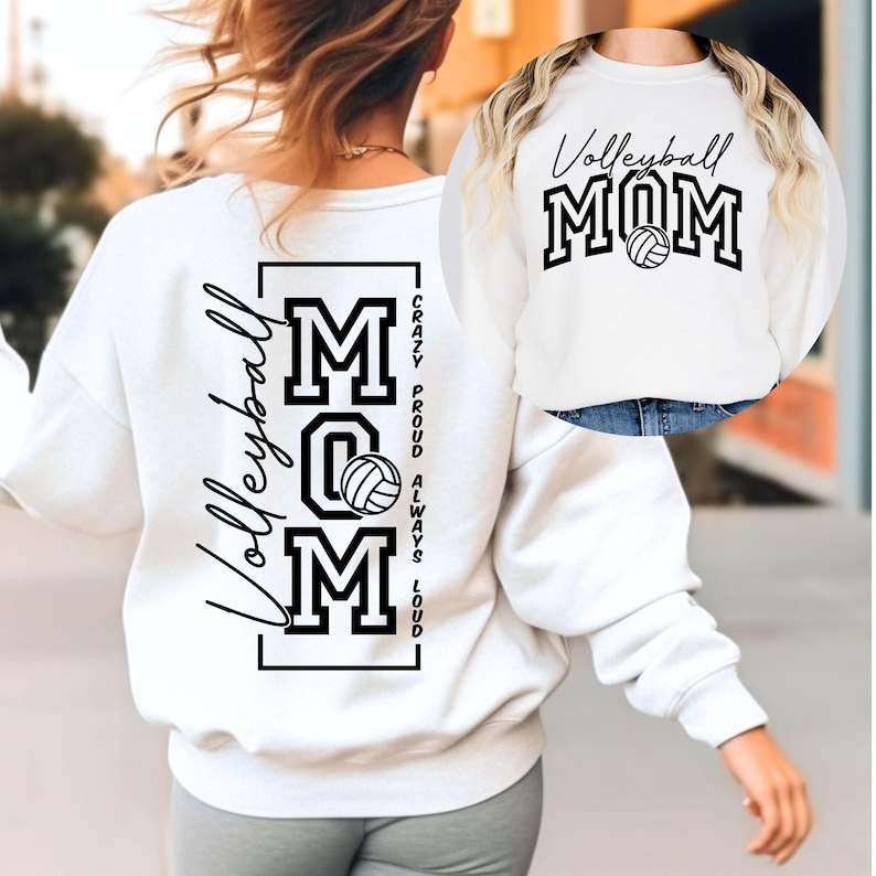 Op de afbeelding: Witte sweatshirt met de tekst "Volleyball MOM" in zwart, met een volleybalafbeelding. De achterkant van de sweatshirt heeft het woord "Volleyball" in script en de woorden "MOM" met een volleybalafbeelding.