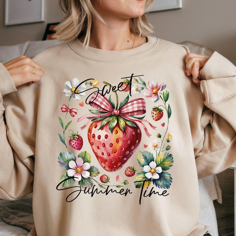 K&ouml;nnte beinhalten: Beiges Sweatshirt mit Aquarelldesign einer Erdbeere, Vichy-Schleife, Blumen und dem Schriftzug "Sweet Summer Time". Ein sommerliches, florales Design.