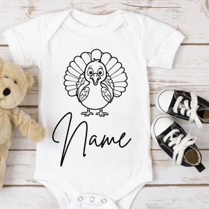 May include: White baby onesie with a black and white cartoon turkey design and the word "Name" printed below.