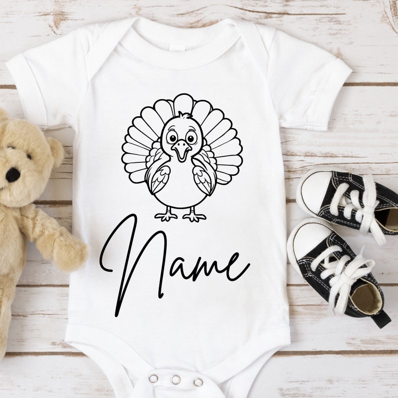 May include: White baby onesie with a black and white cartoon turkey design and the word "Name" printed below.