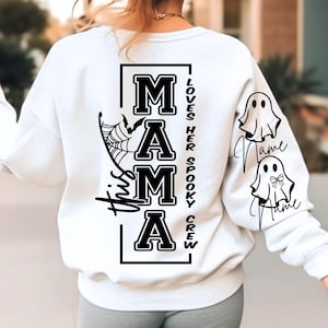 K&ouml;nnte beinhalten: Wei&szlig;es Sweatshirt mit schwarzem Text und Grafiken. Auf der R&uuml;ckseite steht das Wort "MAMA" in fetter Schrift, ein Spinnennetz und eine Fledermaus. Der Text "This Mama Loves Her Spooky Crew" wird ebenfalls angezeigt. Die &Auml;rmel haben Geistergrafiken.