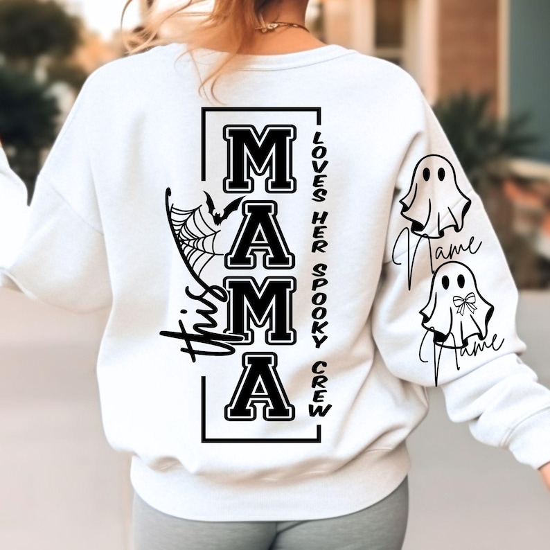 K&ouml;nnte beinhalten: Wei&szlig;es Sweatshirt mit schwarzem Text und Grafiken. Auf der R&uuml;ckseite steht das Wort "MAMA" in fetter Schrift, ein Spinnennetz und eine Fledermaus. Der Text "This Mama Loves Her Spooky Crew" wird ebenfalls angezeigt. Die &Auml;rmel haben Geistergrafiken.