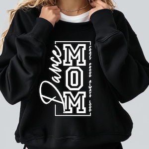 Pode incluir: Camisola de moletom preta com um gr&aacute;fico branco que diz "Dance Mom" com as letras "MOM" em uma fonte grande e em negrito. O texto "Crazy Proud Always Loud" est&aacute; escrito verticalmente do lado direito do gr&aacute;fico.
