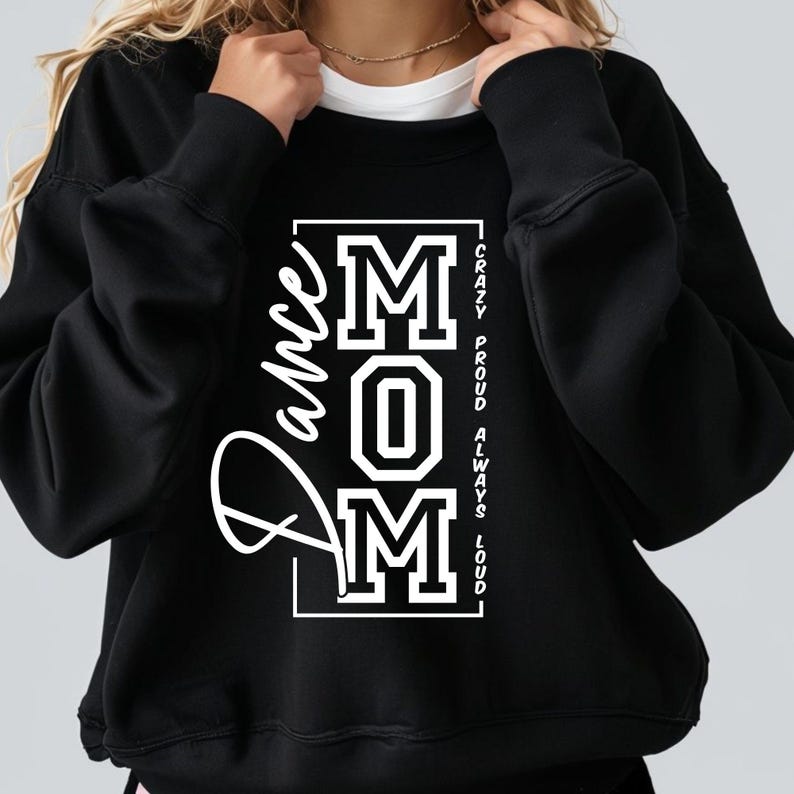 Pode incluir: Camisola de moletom preta com um gr&aacute;fico branco que diz "Dance Mom" com as letras "MOM" em uma fonte grande e em negrito. O texto "Crazy Proud Always Loud" est&aacute; escrito verticalmente do lado direito do gr&aacute;fico.