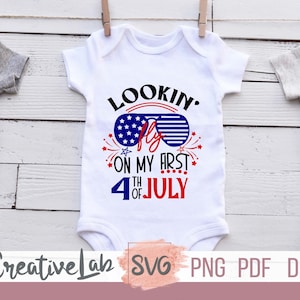 May include: White baby onesie with the text "Lookin' Fly on my First 4th of July" in red, white, and blue. The design includes sunglasses with a stars and stripes pattern and fireworks. The onesie is hanging on a clothesline.