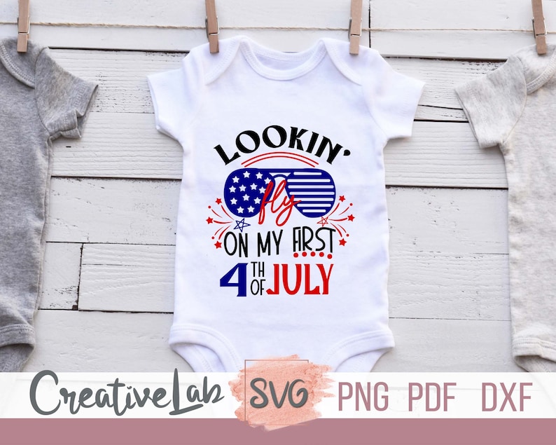 May include: White baby onesie with the text "Lookin' Fly on my First 4th of July" in red, white, and blue. The design includes sunglasses with a stars and stripes pattern and fireworks. The onesie is hanging on a clothesline.