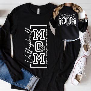 Op de afbeelding: Zwart shirt met lange mouwen met de witte woorden "Volleyball MOM" en een volleybalafbeelding. Het shirt heeft ook de witte zinnen "Crazy, Proud, Always, Loud". Een tweede shirt met de woorden "Volleyball MOM" is ook zichtbaar.