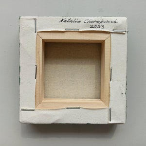 May include: The back of a small, green canvas painting with a wooden frame. The canvas is stapled to the frame and the artist's signature, "Natalia Cherepovick 2023", is written in black ink on the top of the frame.