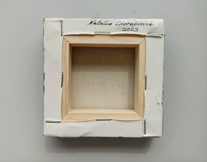May include: The back of a small, green canvas painting with a wooden frame. The canvas is stapled to the frame and the artist's signature, "Natalia Cherepovick 2023", is written in black ink on the top of the frame.