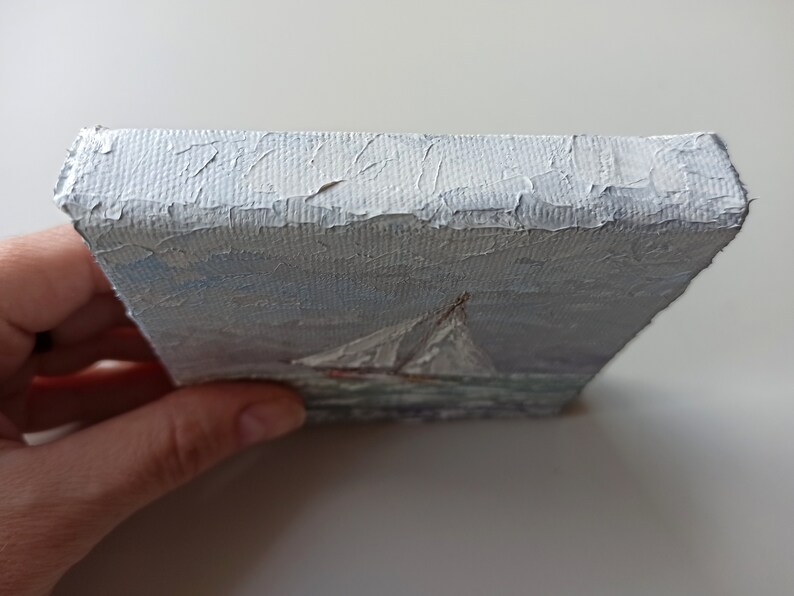 May include: A small, white canvas painting of a sailboat on the water. The painting is done in a loose, impressionistic style, with visible brushstrokes. The sailboat is white with a red hull, and the water is a light blue.
