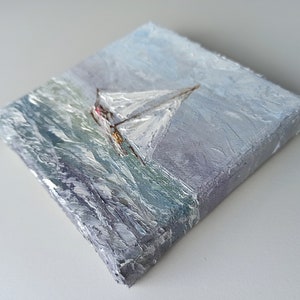 May include: A small oil painting on canvas depicting a sailboat with white sails on a stormy sea. The painting has a textured surface and a blue, gray, and white color scheme.