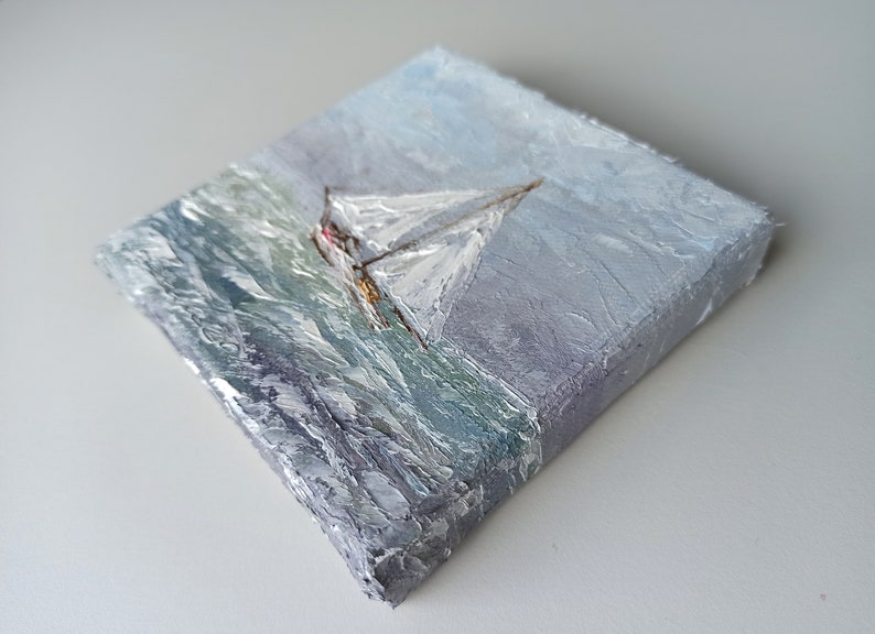 May include: A small oil painting on canvas depicting a sailboat with white sails on a stormy sea. The painting has a textured surface and a blue, gray, and white color scheme.