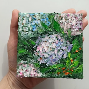 May include: A small painting of hydrangeas in shades of blue, pink, and purple. The flowers are painted with thick, textured strokes, and the background is a deep green.