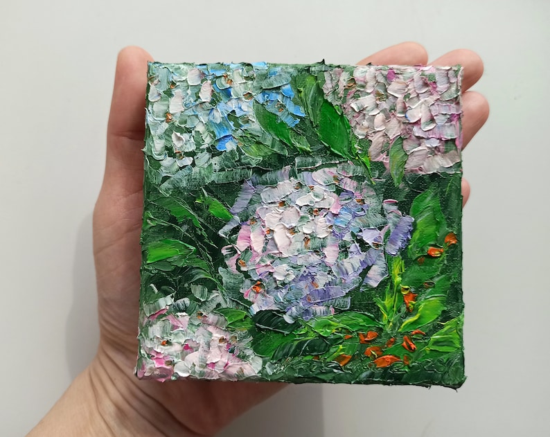 May include: A small painting of hydrangeas in shades of blue, pink, and purple. The flowers are painted with thick, textured strokes, and the background is a deep green.