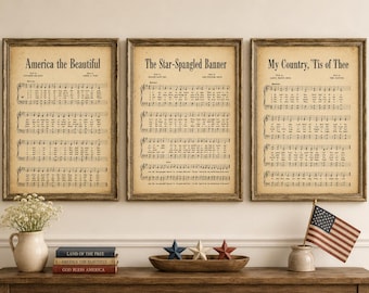 May include: Three framed prints of patriotic sheet music: "America the Beautiful," "The Star-Spangled Banner," and "My Country, 'Tis of Thee." The prints are displayed above a wooden table with decorative items, including books and a small American flag.