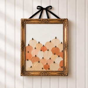 May include: A rectangular wall art piece featuring a collection of textured, impasto-style pumpkins in shades of cream, beige, and orange. The artwork is encased in an ornate, antique gold frame and hangs from a black ribbon tied in a bow.