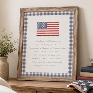 Può includere: Un quadro da parete incorniciato che presenta una bandiera americana ad acquerello e il testo del giuramento di fedeltà. La stampa è bordata da un motivo a quadretti blu e bianchi e racchiusa in una cornice di legno marrone rustico e vissuto.