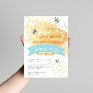 Puede incluir: Una invitaci&oacute;n de baby shower amarilla y azul con un fondo de acuarela y un patr&oacute;n de panal. El texto dice "&iexcl;Nuestro peque&ntilde;o honey est&aacute; cumpliendo un a&ntilde;o!" y "&iexcl;El primer cumplea&ntilde;os de Denver!" La invitaci&oacute;n incluye detalles para la fiesta, incluyendo la fecha, la hora, la ubicaci&oacute;n y la informaci&oacute;n de RSVP.