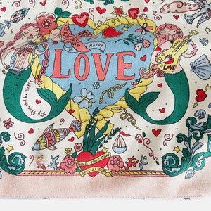 May include: A canvas tote bag with a whimsical design featuring mermaids, hearts, and the word "LOVE" in large letters. The bag has a light pink border and handles with blue and yellow stripes. The overall theme is romantic and nautical.