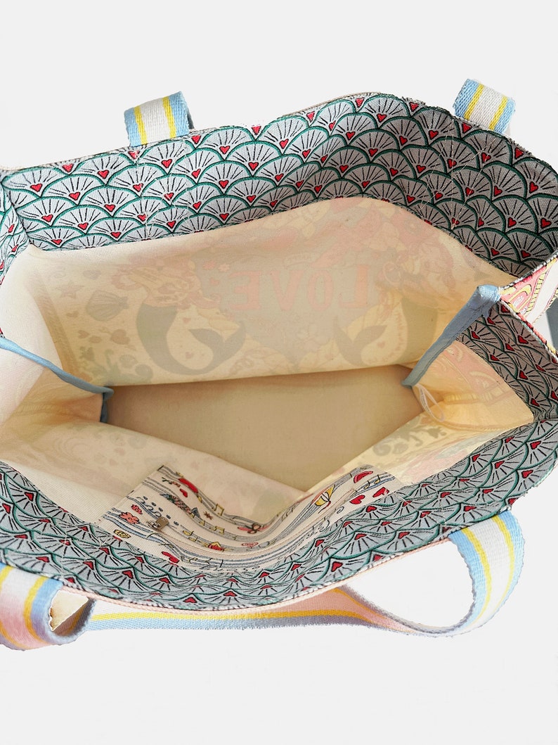 May include: Open view of a tote bag with a patterned exterior and interior. The exterior features a repeating fan design with red hearts. The interior has a floral pattern. The straps are striped with pastel colors.