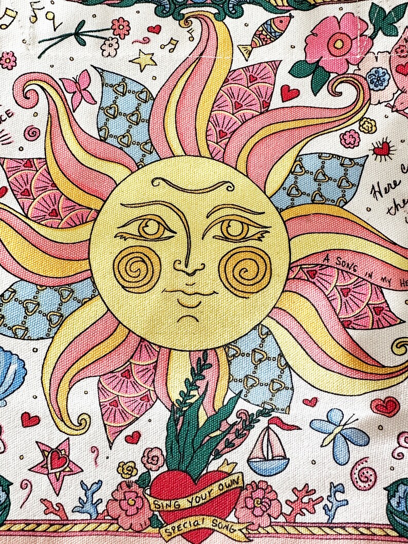 May include: A colorful illustration featuring a smiling sun with rays in shades of yellow, pink, and peach. The design includes hearts, flowers, a sailboat, and the text "SING YOUR OWN SPECIAL SONG". The artwork has a whimsical, folk art style.