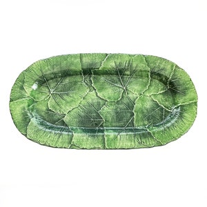 May include: An oval-shaped ceramic serving platter featuring a textured surface composed of overlapping green leaves. The design displays detailed veining and a glossy finish, with varying shades of green creating a realistic botanical appearance.