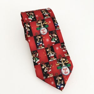 May include: A red and black necktie featuring a repeating pattern of cartoon dogs dressed in Santa hats playing musical instruments. The design includes white snowflakes, musical notes, and circular drum logos with the text Rock n Roll.