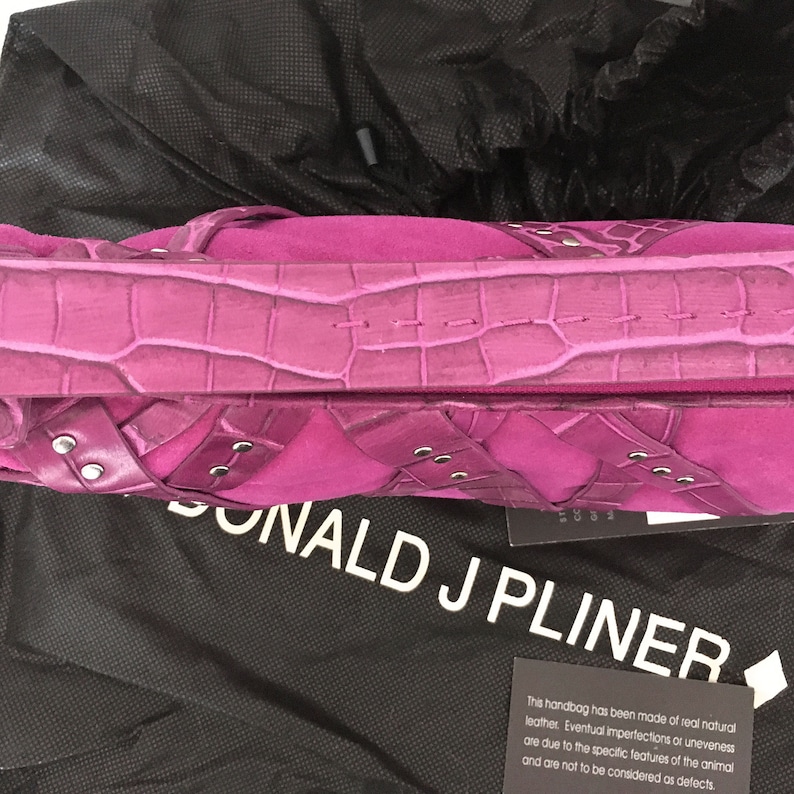 May include: A magenta handbag with a crocodile-textured top and suede-like panels. The bag has silver-toned rivets and a matching handle. The brand name "DONALD J PLINER" is visible on a black dust bag.